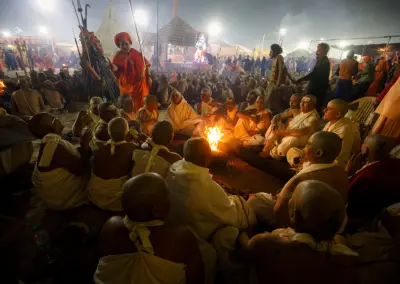 A group of Naga Sadhvis also called “Maata” are sitting in front of a fire during a mass initiation ceremony. In the community of Naga Sadhus, both men and women are present. However, female Naga Sadhus are rare and seldom interact with the world. Women become Naga Sadhus after rigorous penance. For this, they have to perform the same rigorous reparation for years, offer Pind Daan while they are still alive, shave their heads, and then go somewhere and become a female Naga Sadhu. Female Naga Sadhus live secluded lives in forests, caves, and mountains, dedicating themselves to the worship of God. Unlike male Naga Sadhus, female Naga Sadhus do not practice nudity; instead, they wear saffron-colored clothes. They live like other Naga Sadhus, but instead of remaining without clothes, they also wear saffron-colored clothes. The cloth worn by female Naga Sadhus is unstitched and used to cover their bodies. Female Naga Sadhus are also known for their strict adherence to celibacy and ascetic practices, just like their male counterparts. Despite the challenges they face, these women continue to pursue spiritual enlightenment and dedicate their lives to serving a higher purpose.
