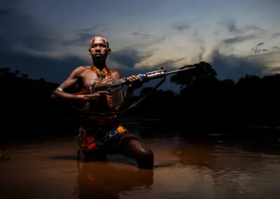 Portrait of a Karo tribe man in the Omo Valley, Ethiopia, holding a Kalashnikov rifle in a river, with ceremonial body paint.