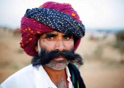 Close-up portrait of a Rajasthani camel trader wearing a red-and-black turban with a large moustache at the Pushkar fair.